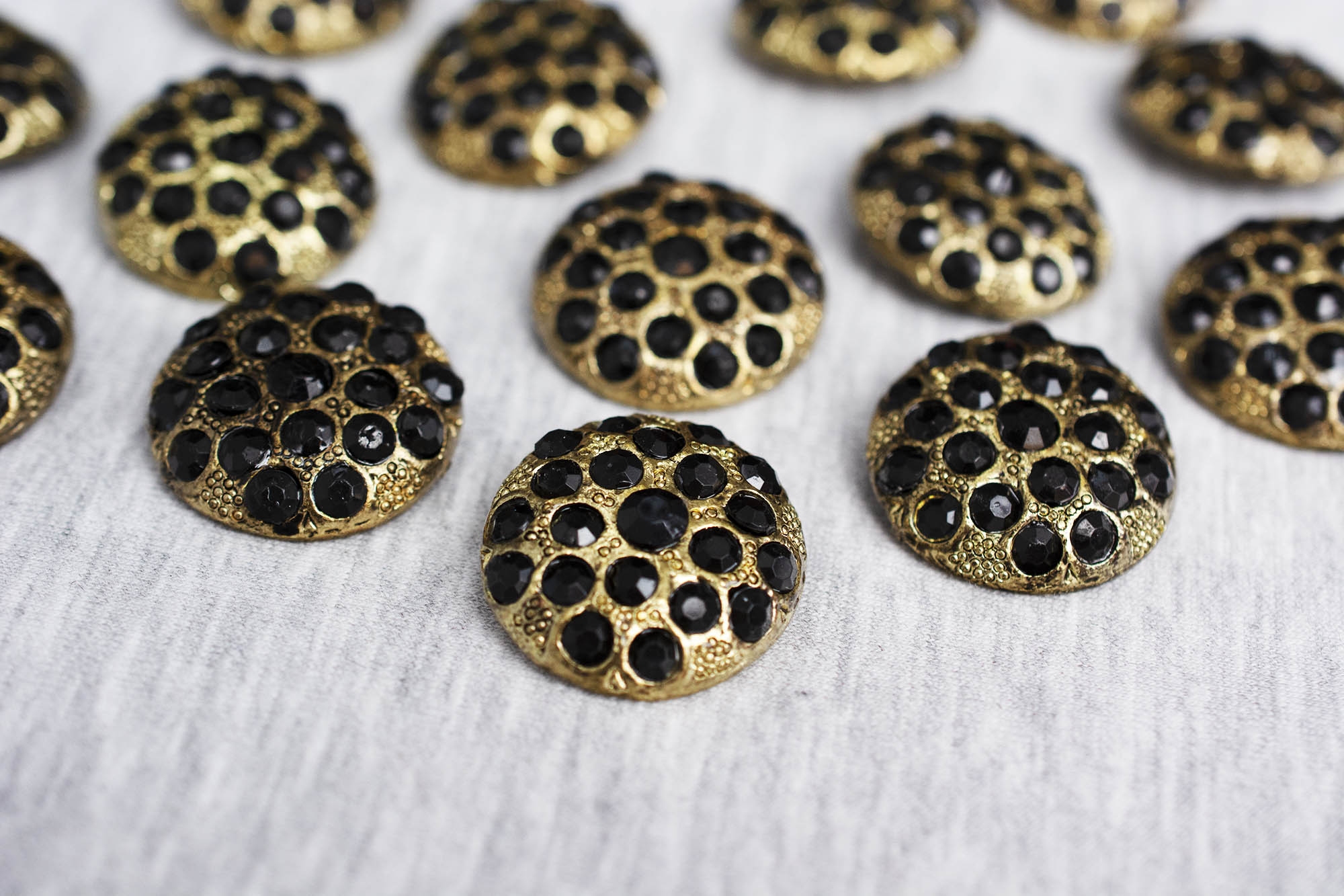 Pozłacany metalowy guzik na stopce, ozdobiony czarnymi kryształkami, o szerokości 2,5 cm.