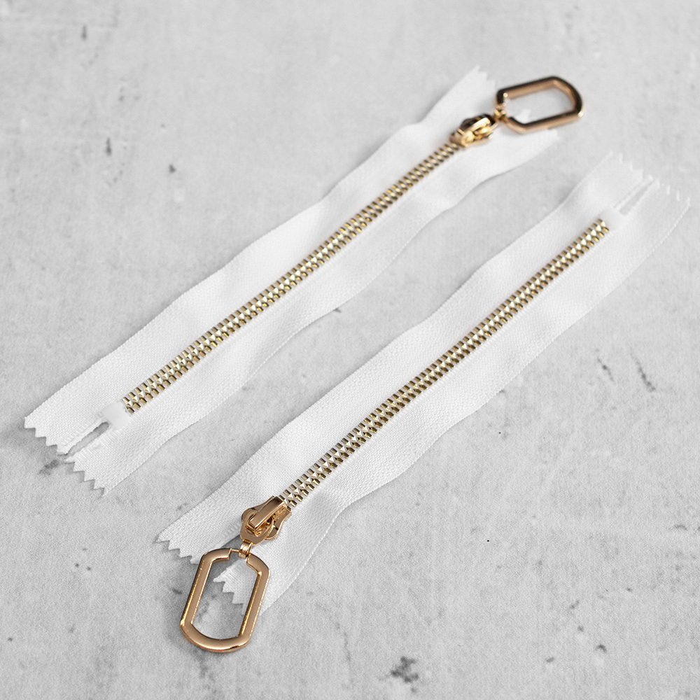 Zamek plastikowy typu kostka z eleganckimi, pozłacanymi ząbkami i ozdobnym kółkiem na suwaku.