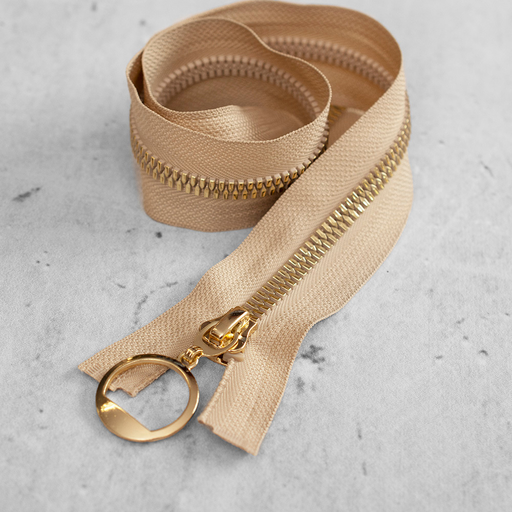 Zamek plastikowy typu kostka z eleganckimi, pozłacanymi ząbkami i ozdobną zawieszką&nbsp;na suwaku.