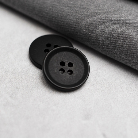 Plastikowy guzik garniturowy w kolorze czarnym o średnicy 2 cm, przyszywany na cztery dziurki.
