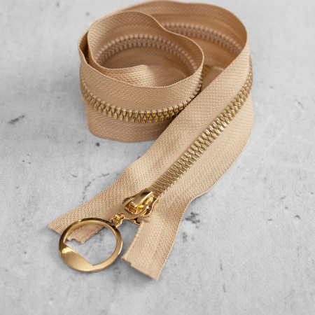 Zamek plastikowy typu kostka z eleganckimi, pozłacanymi ząbkami i ozdobną zawieszką&nbsp;na suwaku.