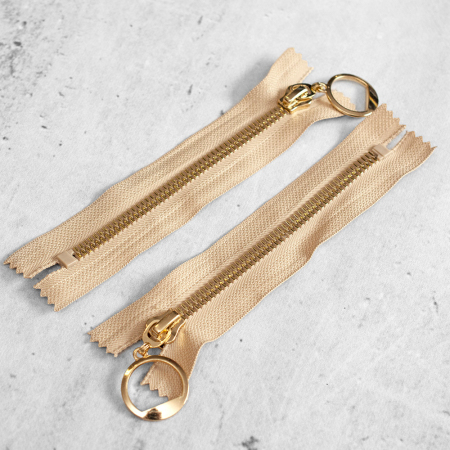 Zamek plastikowy typu kostka z eleganckimi, pozłacanymi ząbkami i ozdobną zawieszką&nbsp;na suwaku.