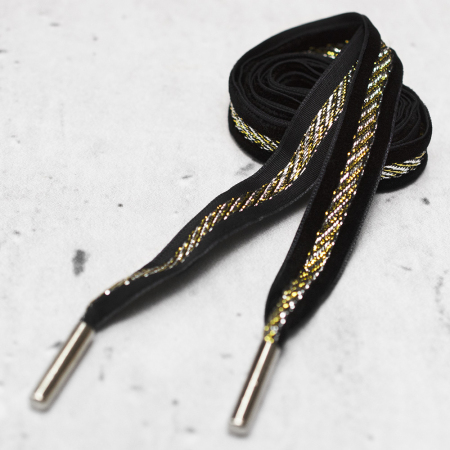 Ozdobny sznurek wykonany z czarnej taśmy z dodatkiem metalowej nici, zakończony z obu stron metalową skuwką.
