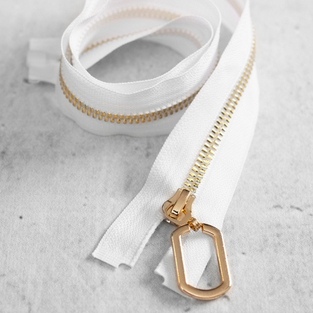 Zamek plastikowy typu kostka z eleganckimi, pozłacanymi ząbkami i ozdobnym kółkiem na suwaku.