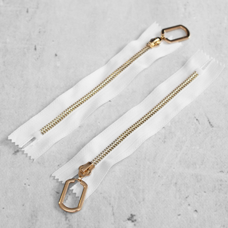 Zamek plastikowy typu kostka z eleganckimi, pozłacanymi ząbkami i ozdobnym kółkiem na suwaku.