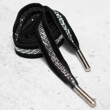 Ozdobny sznurek wykonany z czarnej taśmy z dodatkiem metalowej nici, zakończony z obu stron metalową skuwką.
